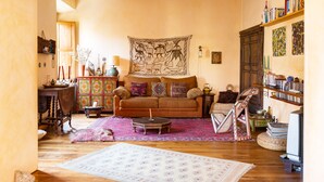 A cozy living room with a wooden floor, a brown sofa, a colorful tapestry, and a bookshelf filled with books and decorative items. - Charming Bright Colosseum (Roma)