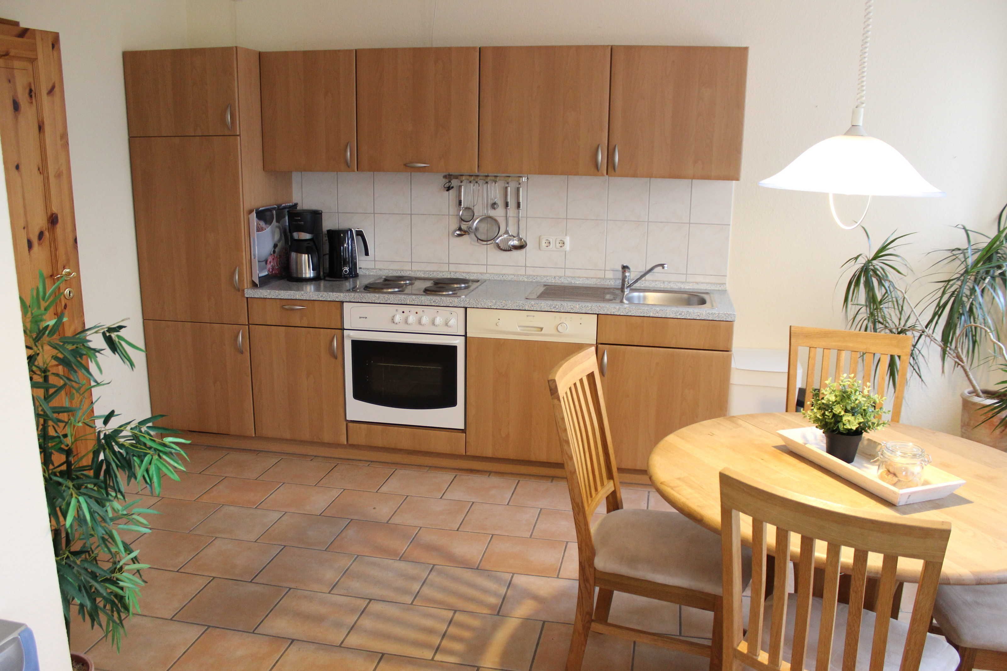 A kitchen with wooden cabinets, a stove, a sink, and a dining area with a table and chairs.