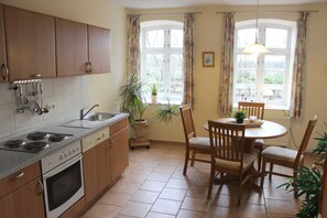 Une cuisine avec des meubles de rangement en bois, une cuisinière et un coin repas comprenant des chaises et une table.