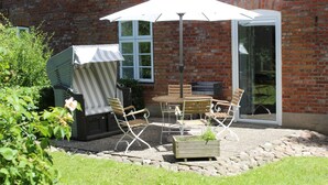 A patio with a table and chairs, a covered grill, and a brick wall. - Vacation apartment Ostseeanleger - OSTSEE-Ferienwohnungen (Hasselberg)