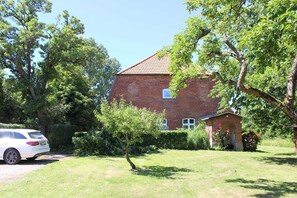 Un bâtiment en briques avec un petit jardin, une voiture garée devant et un arbre au premier plan.