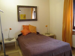 A bedroom with a bed, a nightstand, a mirror, and a lamp. - Vacation apartment Altstadtoase - Ferienw. Old Town Oasis | App: Tillyschanzenblick | (Hann. Münden)