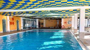 Une piscine intérieure avec un plafond à carreaux, une eau d’un bleu limpide et une bouée de sauvetage sur le côté droit.