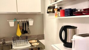 Une cuisine de taille réduite, avec des meubles blancs, une cuisinière, un four à micro-ondes et une bouilloire.