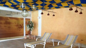 Une pièce avec deux fauteuils confortables, un plafond orné de luminaires suspendus et un mur décoré d’un motif géométrique.