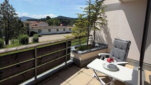 A balcony with a view of buildings and trees, a white table with a chair, and a small planter with plants. - Calm, spacious, sunny apartment with view at the Alps (Scheidegg)
