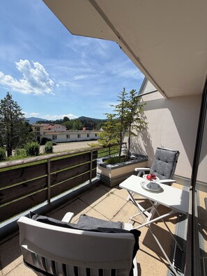 A balcony with a view of buildings and trees, a white table with a chair, and a small planter with plants. - Calm, spacious, sunny apartment with view at the Alps (Scheidegg)