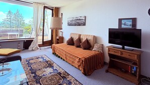 A room with a bed, a TV, a lamp, a window with curtains, and a view of the outdoors. - Calm, spacious, sunny apartment with view at the Alps (Scheidegg)