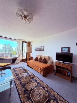 A room with a bed, a TV, a lamp, a window with curtains, and a view of the outdoors. - Calm, spacious, sunny apartment with view at the Alps (Scheidegg)
