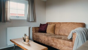 Un salon avec un canapé marron, une table basse en bois et une fenêtre avec des rideaux.