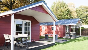 Un bâtiment rouge doté d’un patio couvert, d’une table avec des chaises et d’un petit jardin.