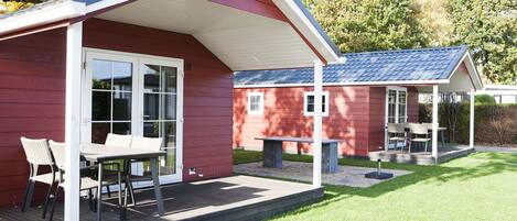 A red building with a covered patio area, a table with chairs, and a small garden.
