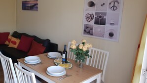 A dining area with a wooden table set for two, white chairs, a vase of yellow roses, and a bottle of wine. - Apartment Benimar with heated pool, large terrace, dishwasher, wifi, SAT-TV (Costa Adeje)