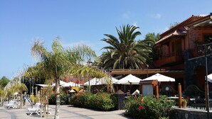 A courtyard with outdoor seating, palm trees, and a building with a tiled roof. - Apartment Benimar with heated pool, large terrace, dishwasher, wifi, SAT-TV (Costa Adeje)