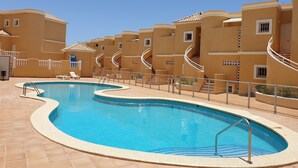 A swimming pool with a curved design, surrounded by a tiled deck and a building with a curved facade and spiral staircases. - Apartment Benimar with heated pool, large terrace, dishwasher, wifi, SAT-TV (Costa Adeje)