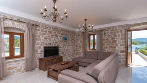 A living room with stone walls, a wooden TV stand, a beige sofa, and a chandelier.