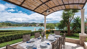 An outdoor dining area with a table set for four, overlooking a body of water and a mountainous landscape.