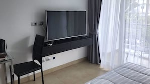 Ein modernes Hotelzimmer mit einem an der Wand montierten Flachbildfernseher, einem schwarzen Sessel, einem Bett und einem großen Fenster mit transparenten Vorhängen.