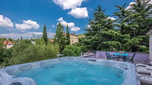 A hot tub with a control panel, surrounded by outdoor furniture and greenery.