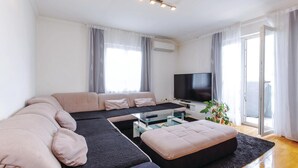 A modern living room with a large L-shaped sofa, a glass coffee table, and a flat-screen TV.