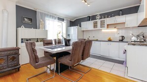 A modern kitchen with white cabinets, a dining table with four chairs, and a refrigerator.