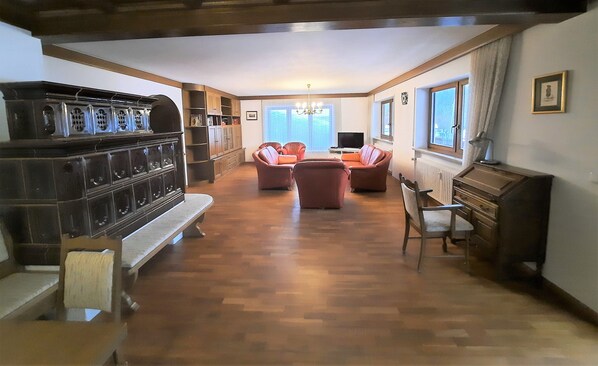 A spacious living room with a wooden floor, a bench, a piano, and a television.