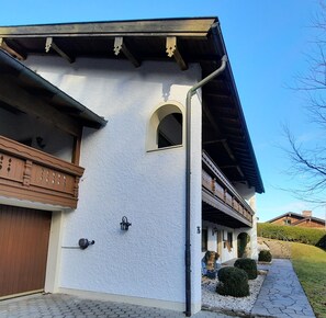 A building with a white exterior, wooden balcony, and a stone pathway leading to the entrance.