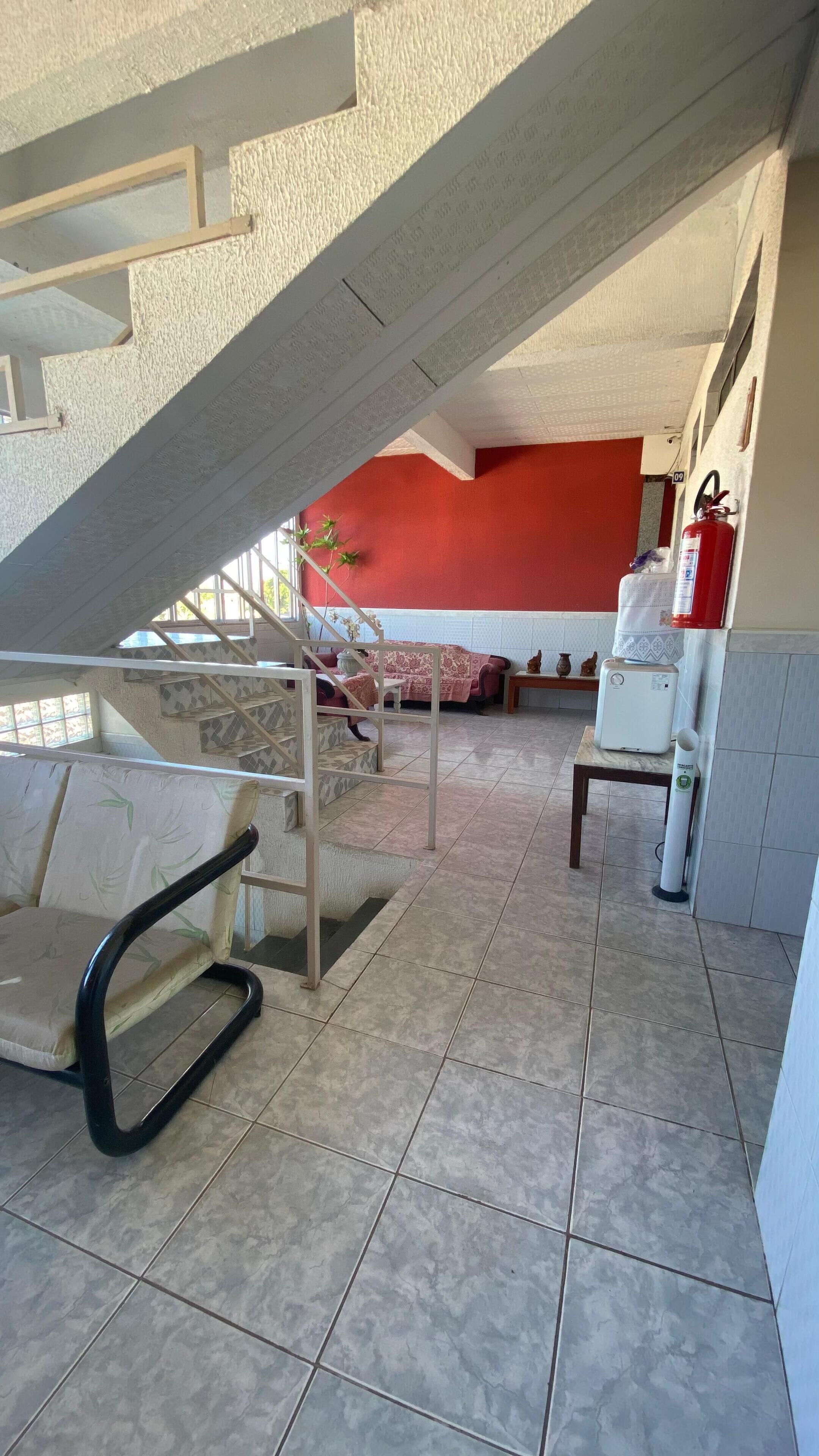 A hotel room with a staircase, a bed with a red wall, a small table, a water dispenser, and a fire extinguisher.