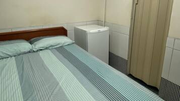 Una habitación pequeña y sencilla con una cama, un ventilador de techo, un calentador blanco y una puerta.