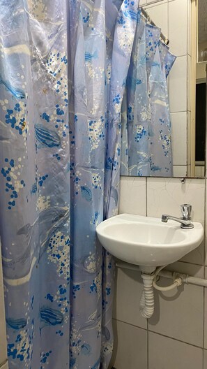 A bathroom with a white sink, a mirror, and a shower curtain with a blue and white pattern. - Pousada e Alojamento do Engenho de Itaguai (Itaguai)