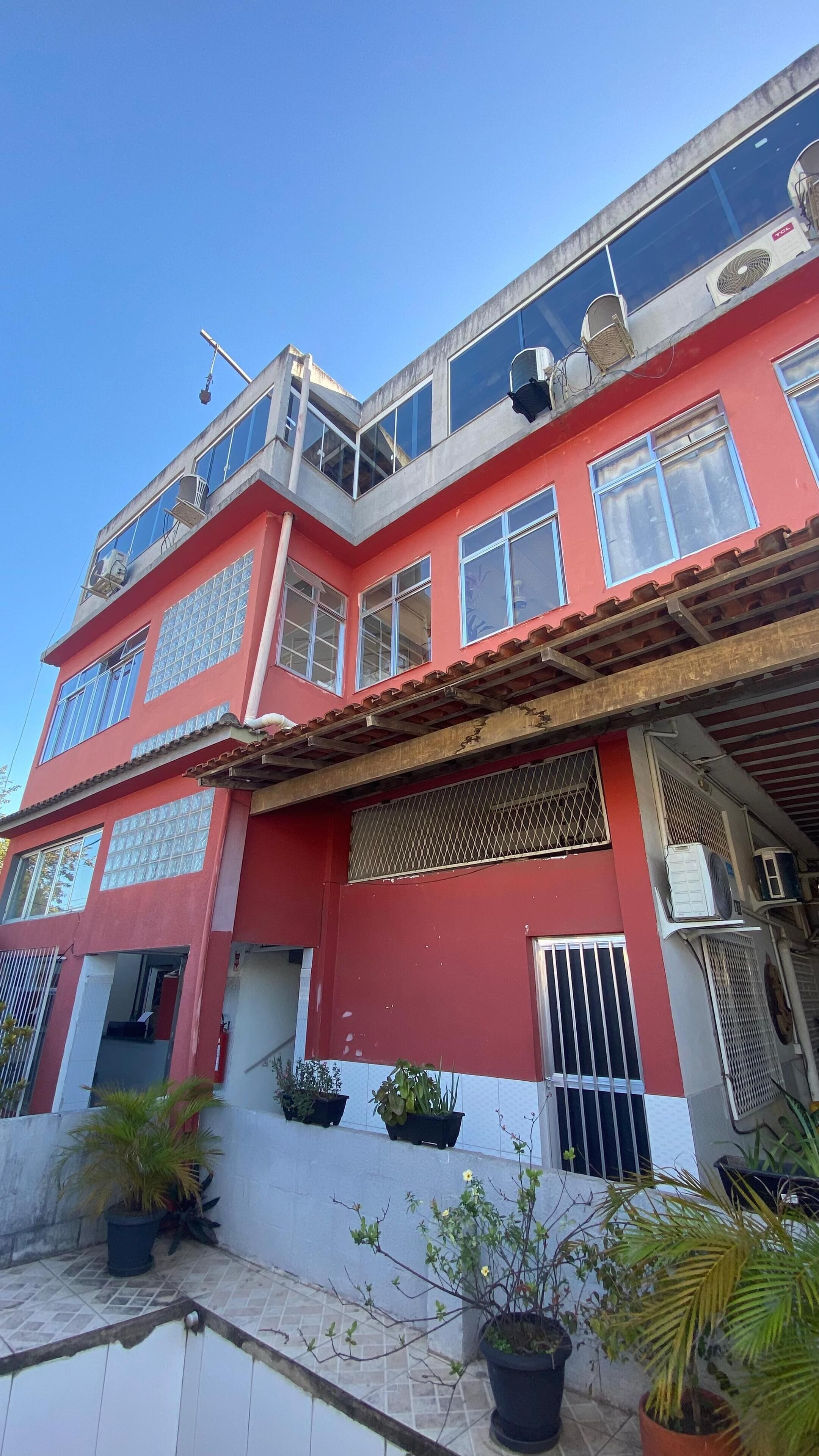 A red building with multiple windows, air conditioning units, and potted plants.