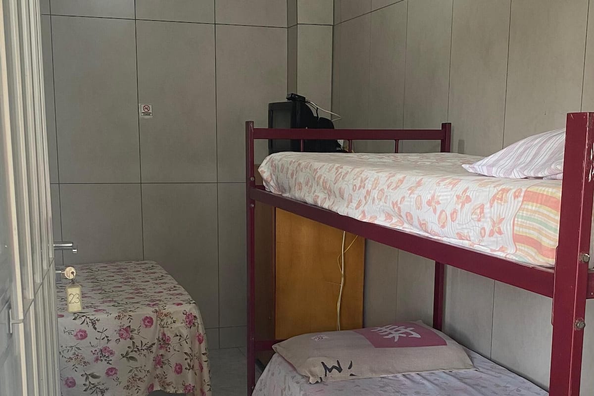 A small, tiled room with two bunk beds, a ceiling fan, and a television on a stand.