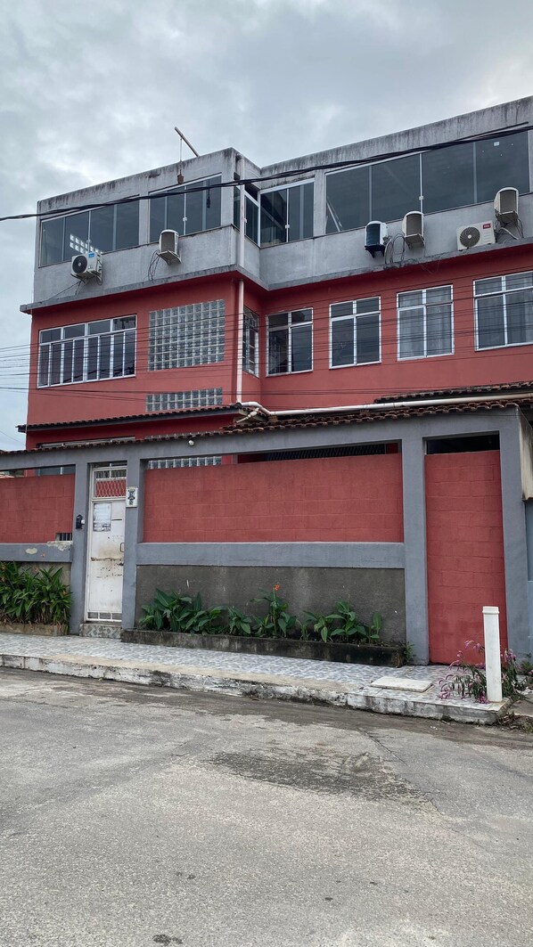 A two-story building with a red and grey facade, multiple windows, and air conditioning units. - Pousada e Alojamento do Engenho de Itaguai (Itaguai)
