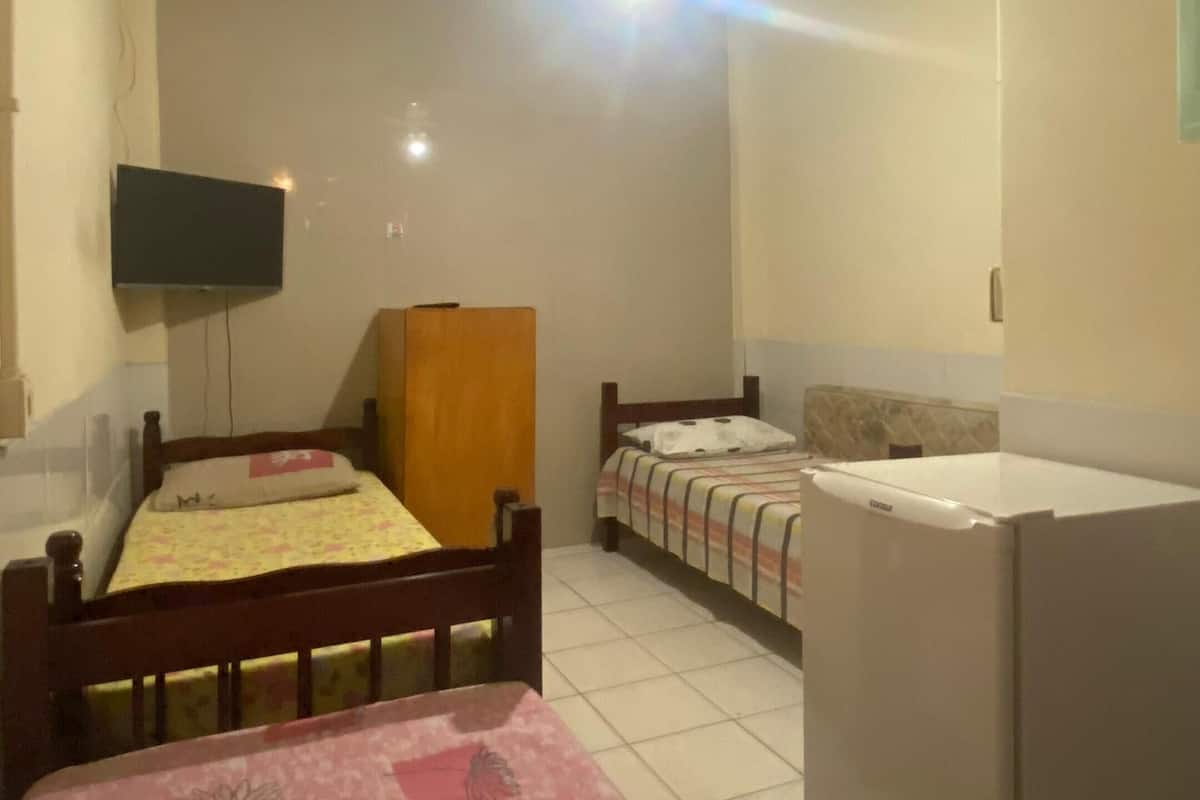 A bedroom with two beds, a ceiling fan, a television, and a refrigerator.