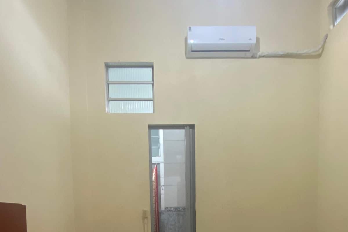 A small, clean room with two single beds, a door leading to a bathroom, and a ceiling fan.