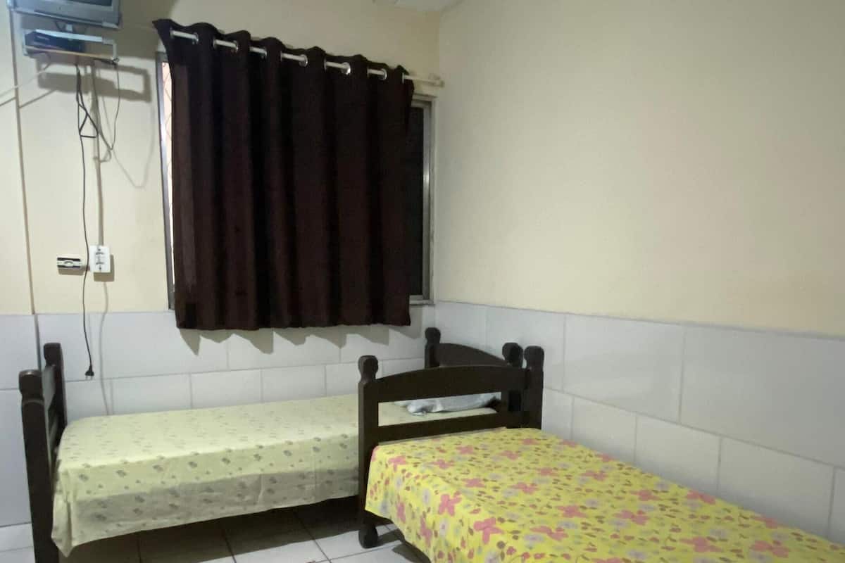 A small room with two single beds, a television mounted on the wall, and a window with curtains.