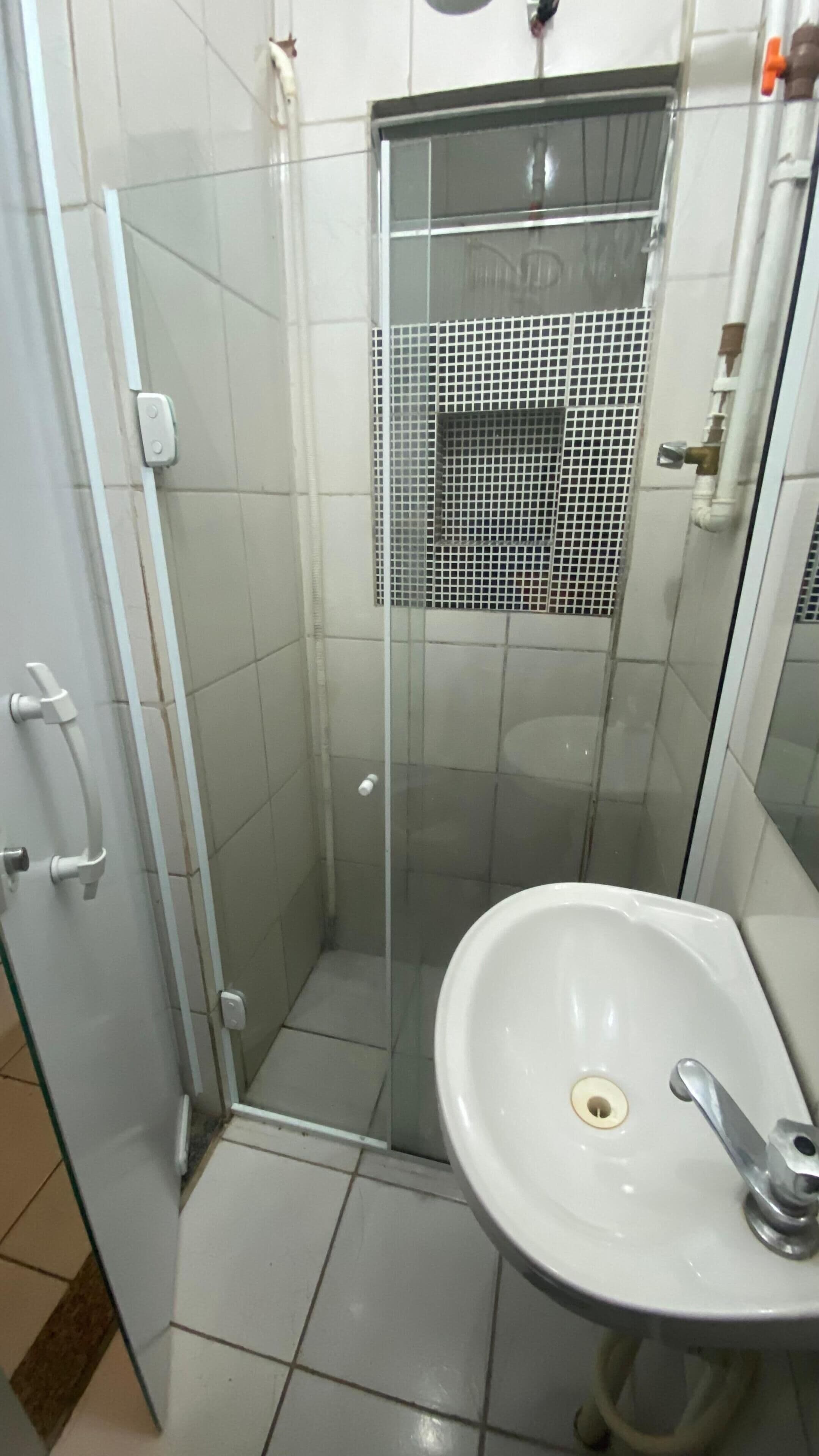 A bathroom with a glass shower enclosure, a white sink, and a tiled floor.