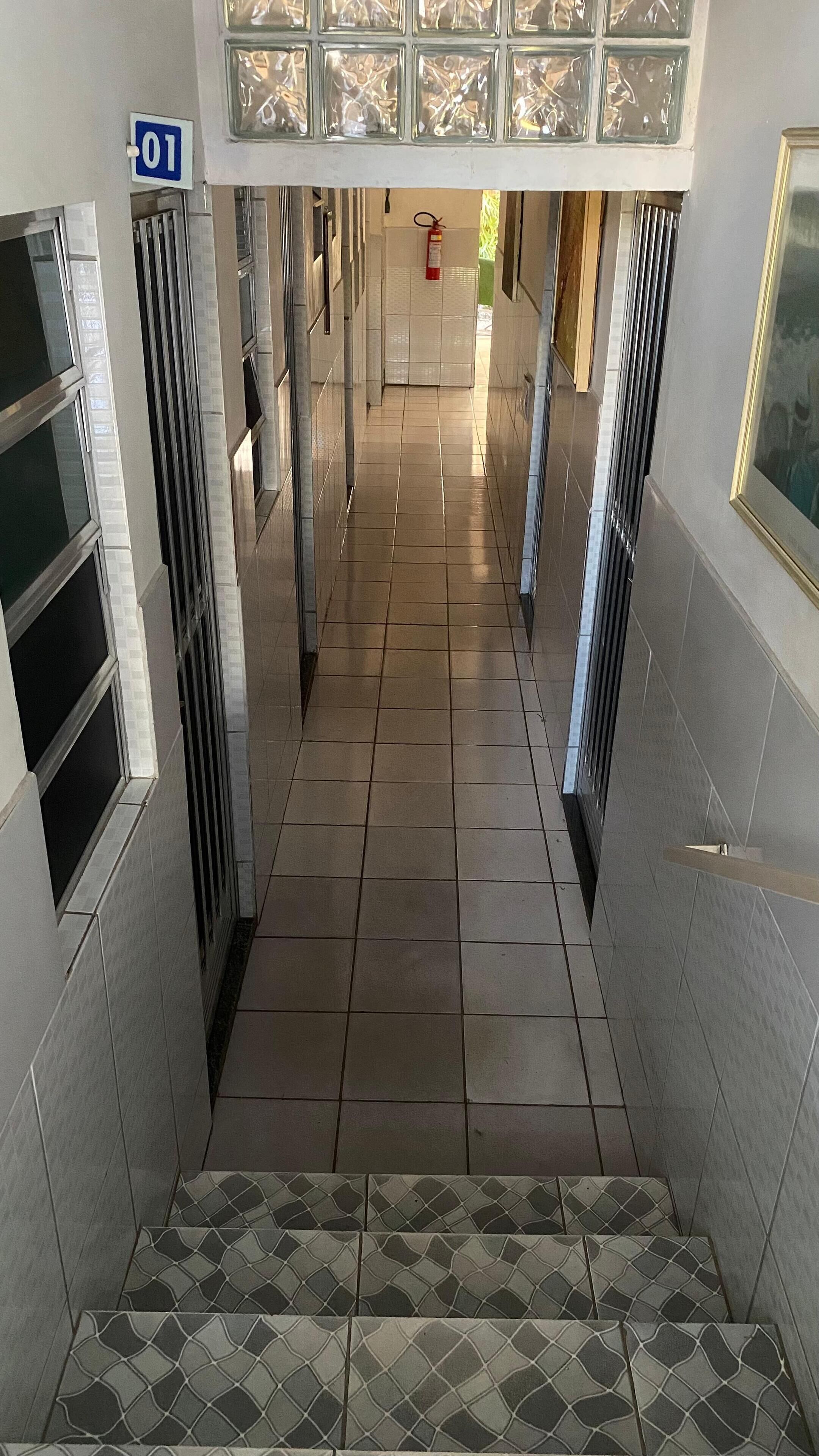 A corridor with tiled floors, a fire extinguisher, and a blue sign indicating room number 01.
