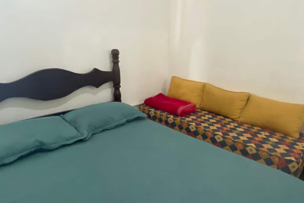 A bedroom with a bed, a nightstand, a lamp, and a patterned sofa.