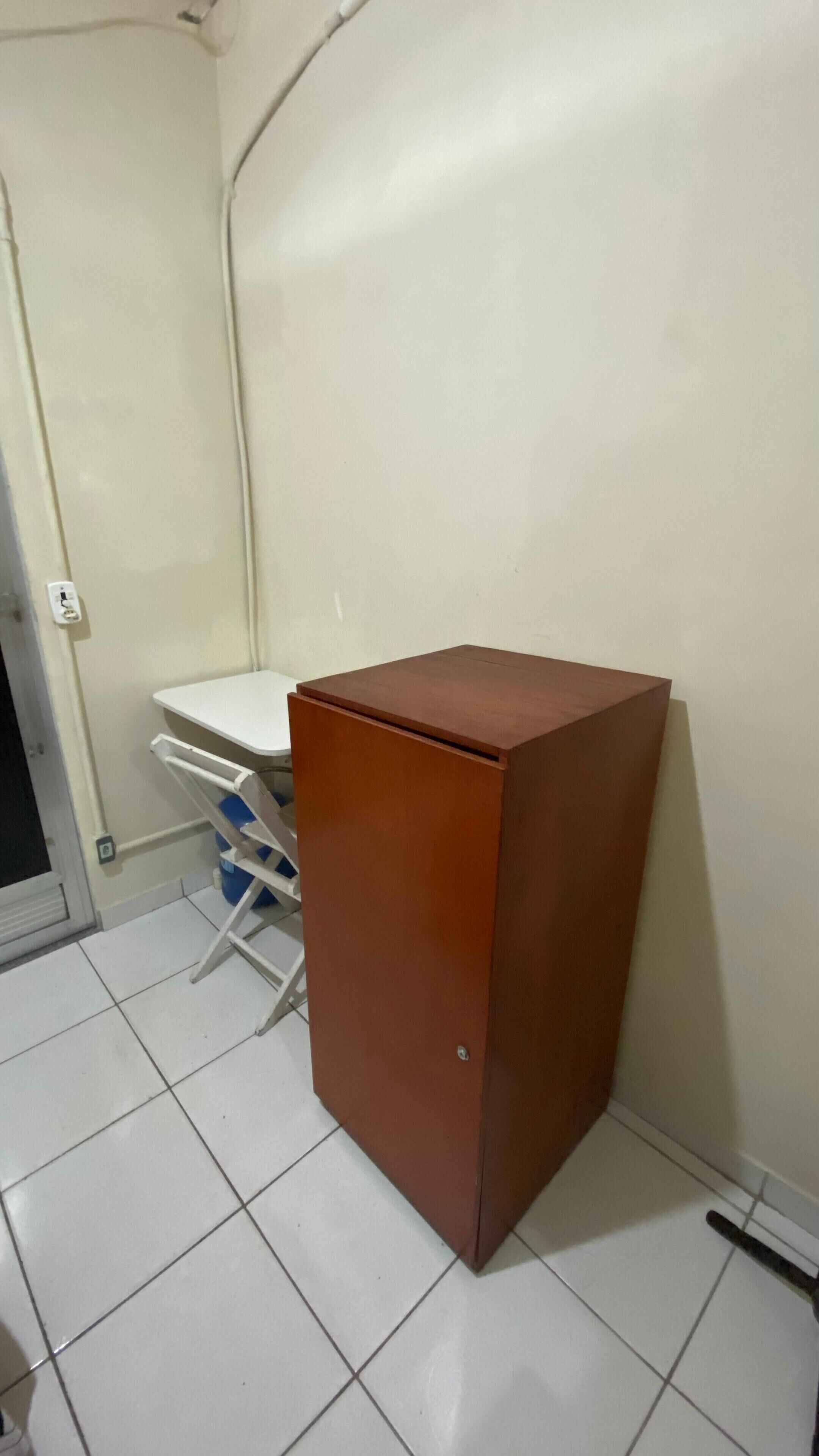 Un mueble pequeño y marrón en una esquina de una habitación con suelo de baldosas blancas y pared blanca.