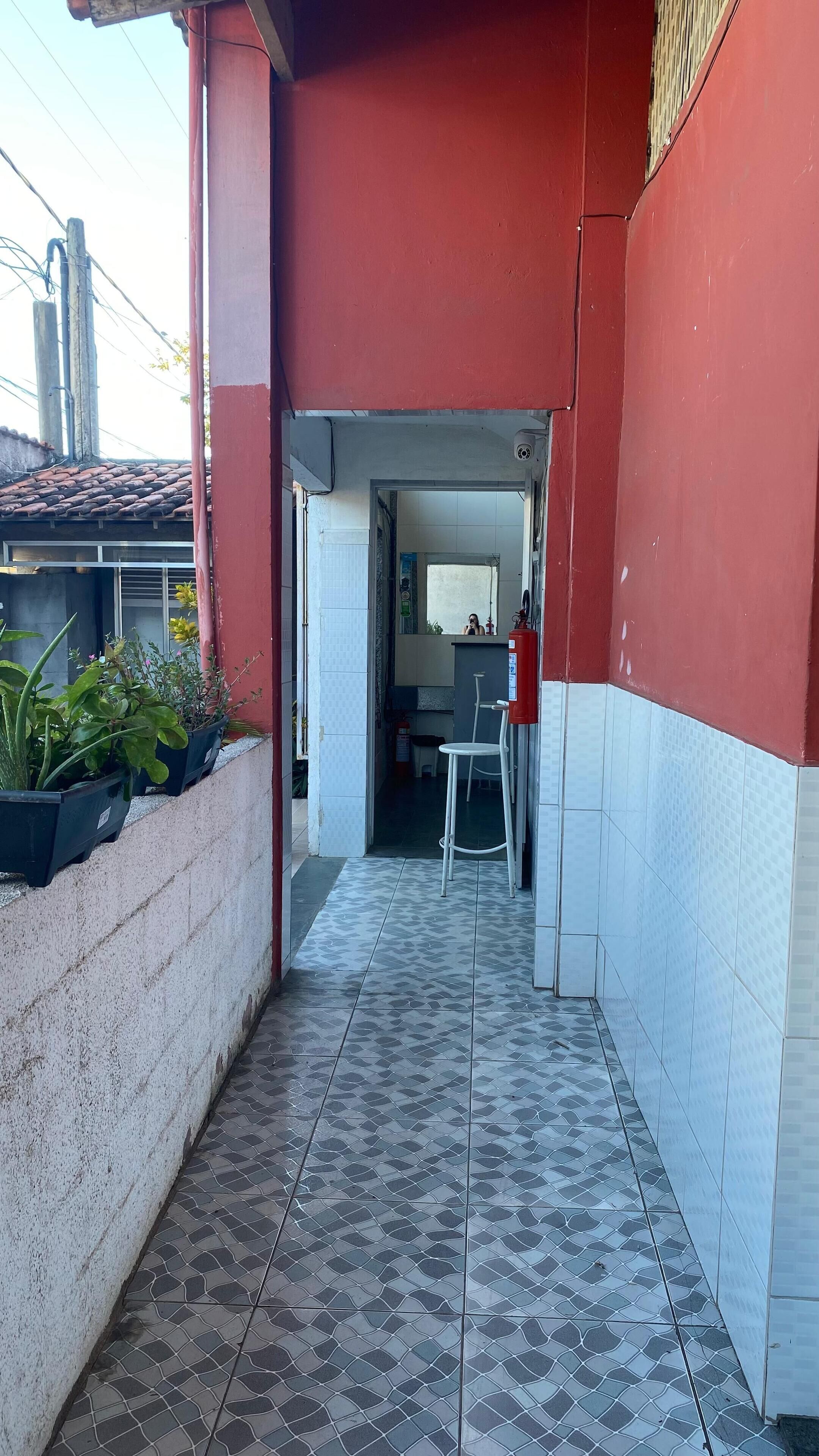 A narrow corridor with tiled flooring, a red wall, and a white tiled wall. There is a white chair and a red fire extinguisher visible.
