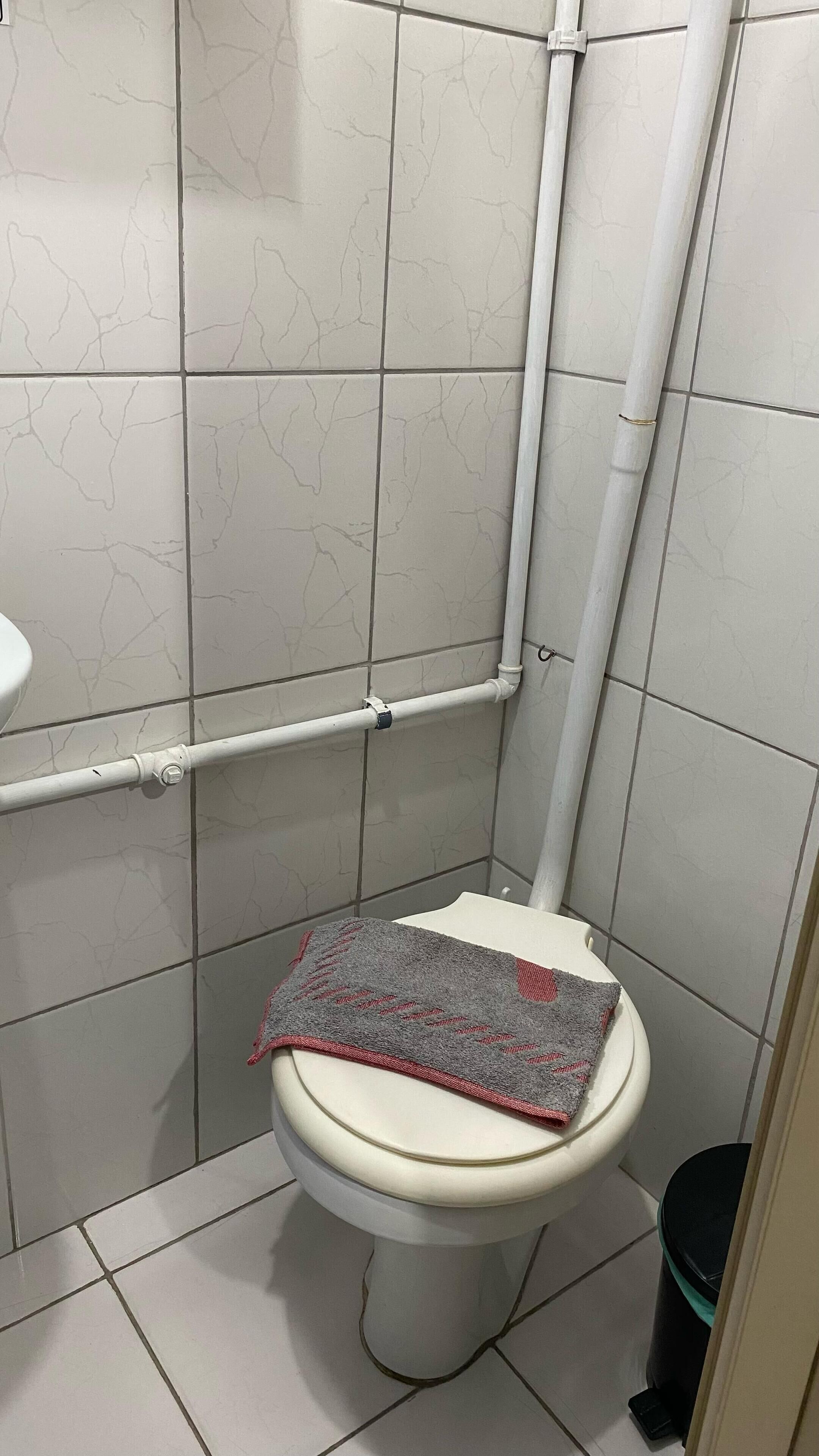 A bathroom with white tiled walls, a white toilet, and a black trash bin.