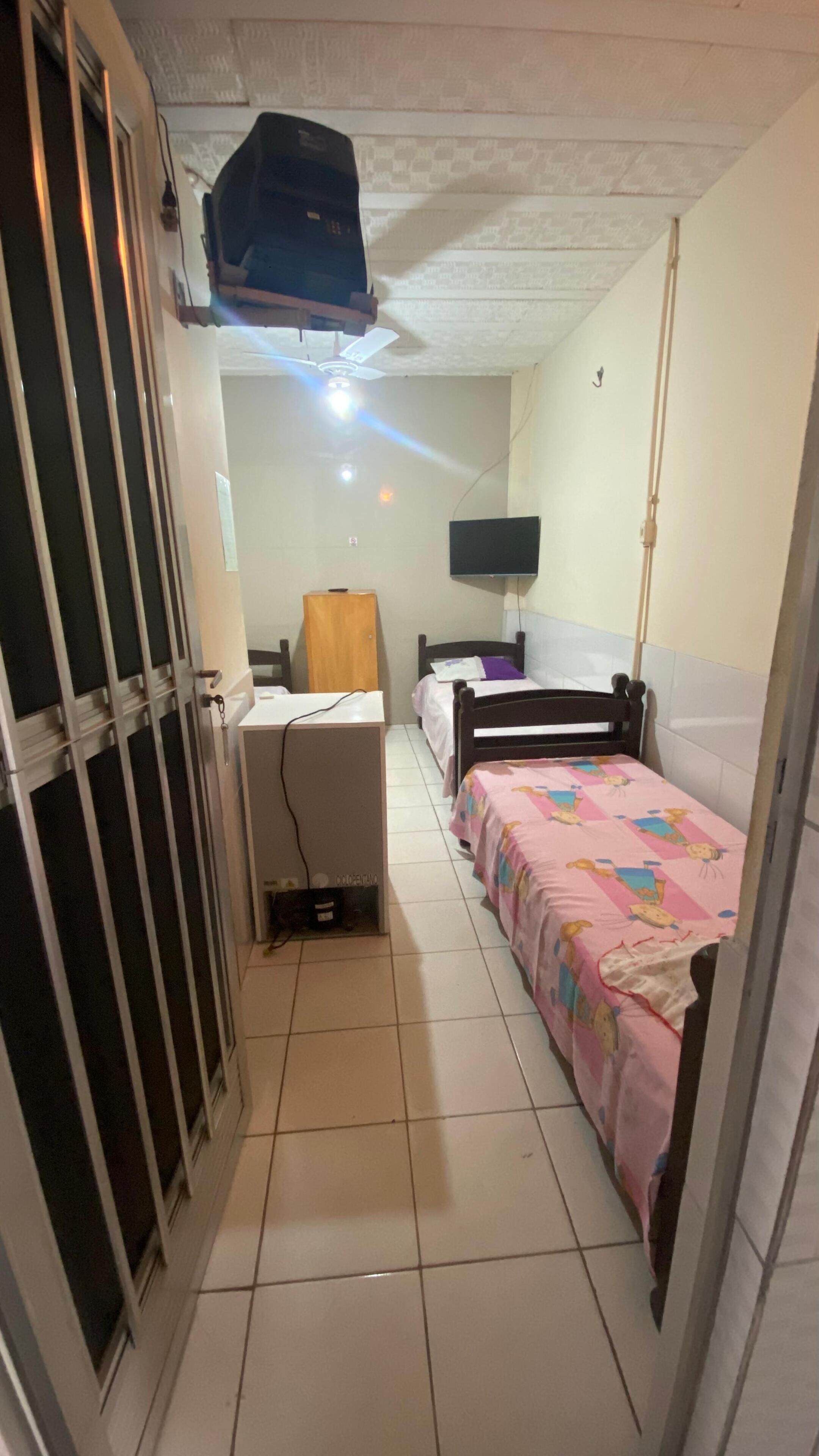 Una habitación pequeña y estrecha con una cama, un escritorio y un televisor en la pared.