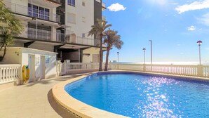 Una piscina con vistas al mar, un edificio con balcones y una palmera.