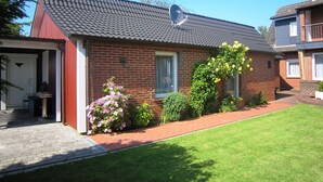 A two-story brick house with a tiled roof, a satellite dish, and a well-maintained garden with various plants and flowers.