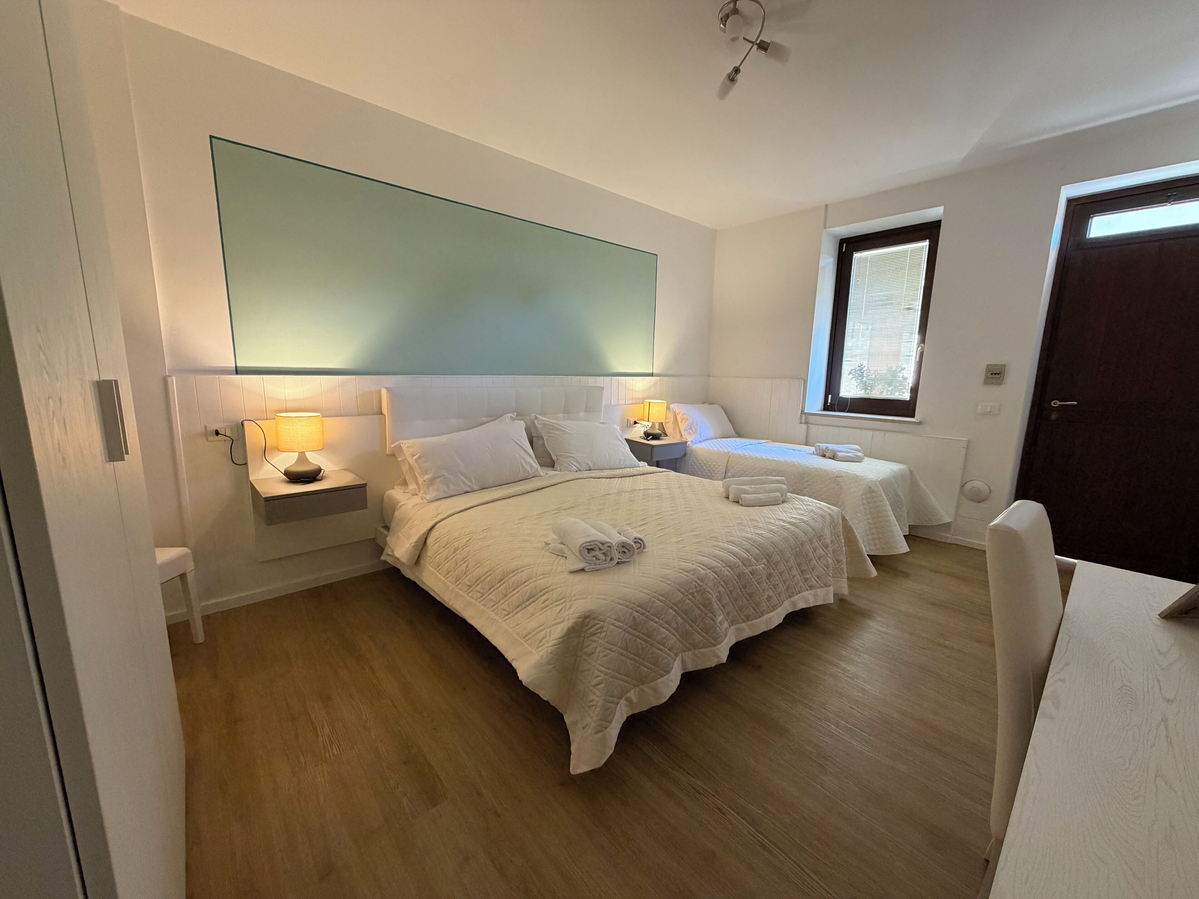 A hotel room with two beds, a large mirror, bedside lamps, a window, and a door.