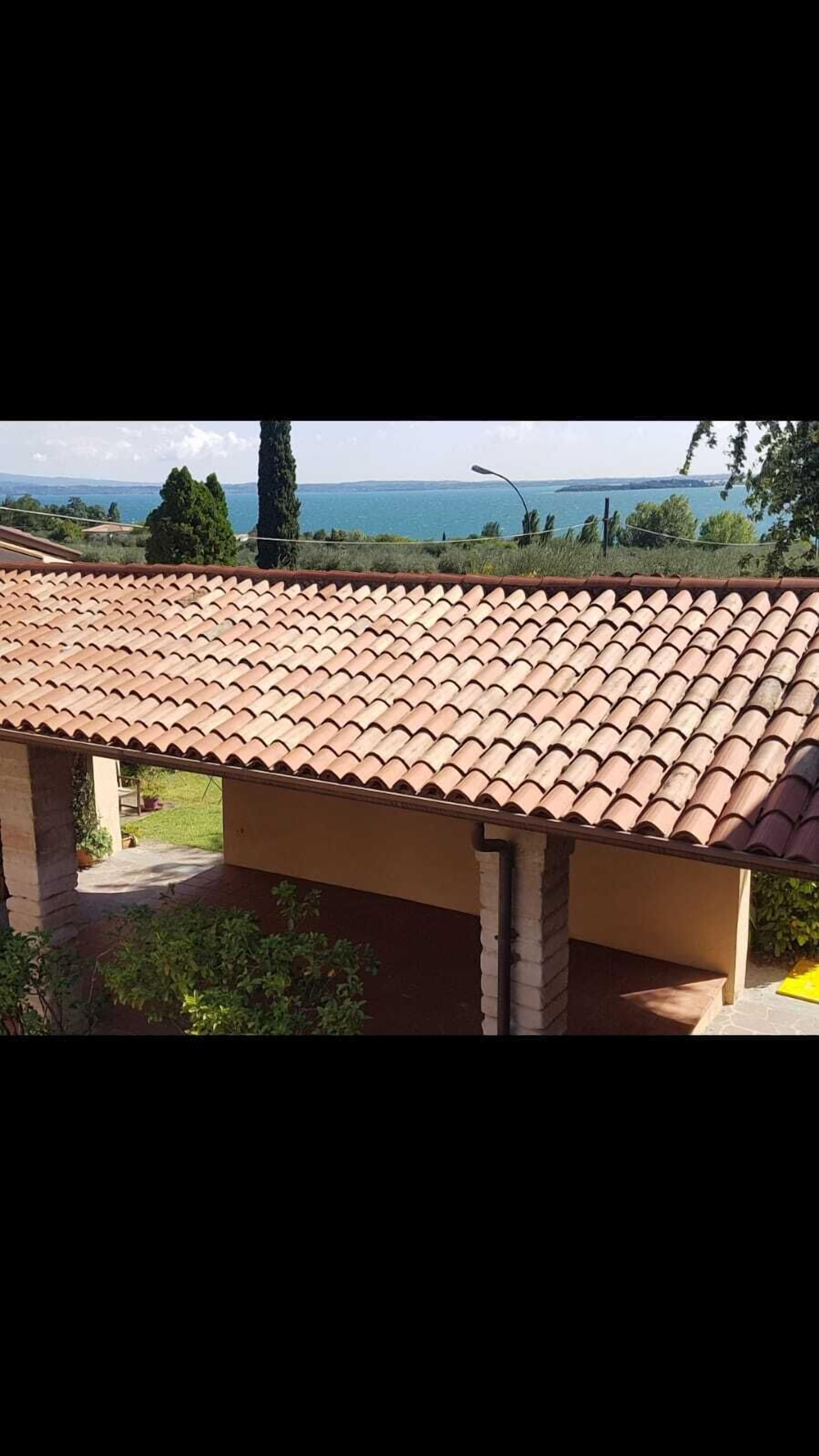 Un edificio de techo de tejas, estructura de ladrillo y vista a una masa de agua y colinas distantes.