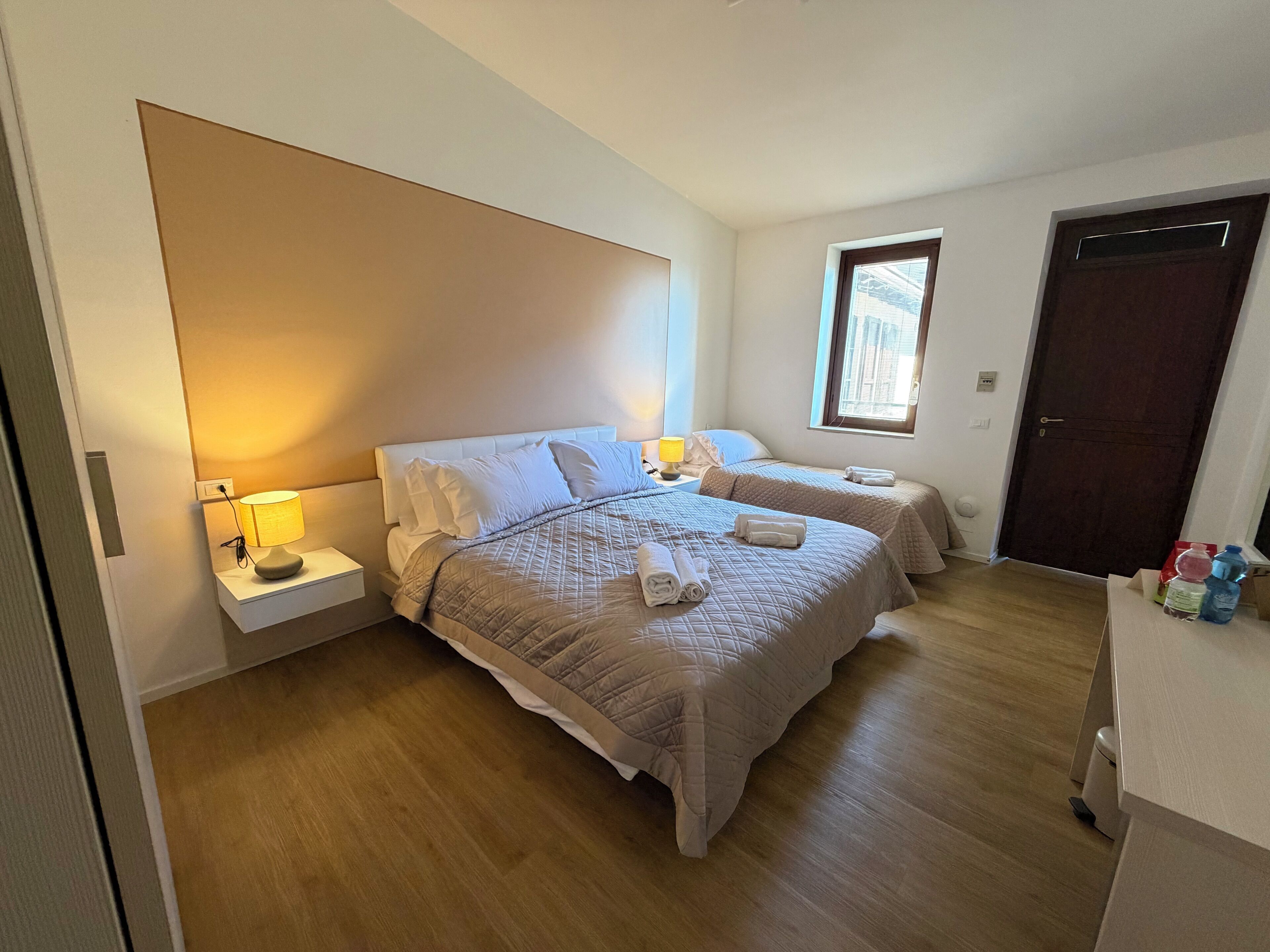 Een slaapkamer met twee bedden, een nachtkastje met een lamp, een raam en een deur.