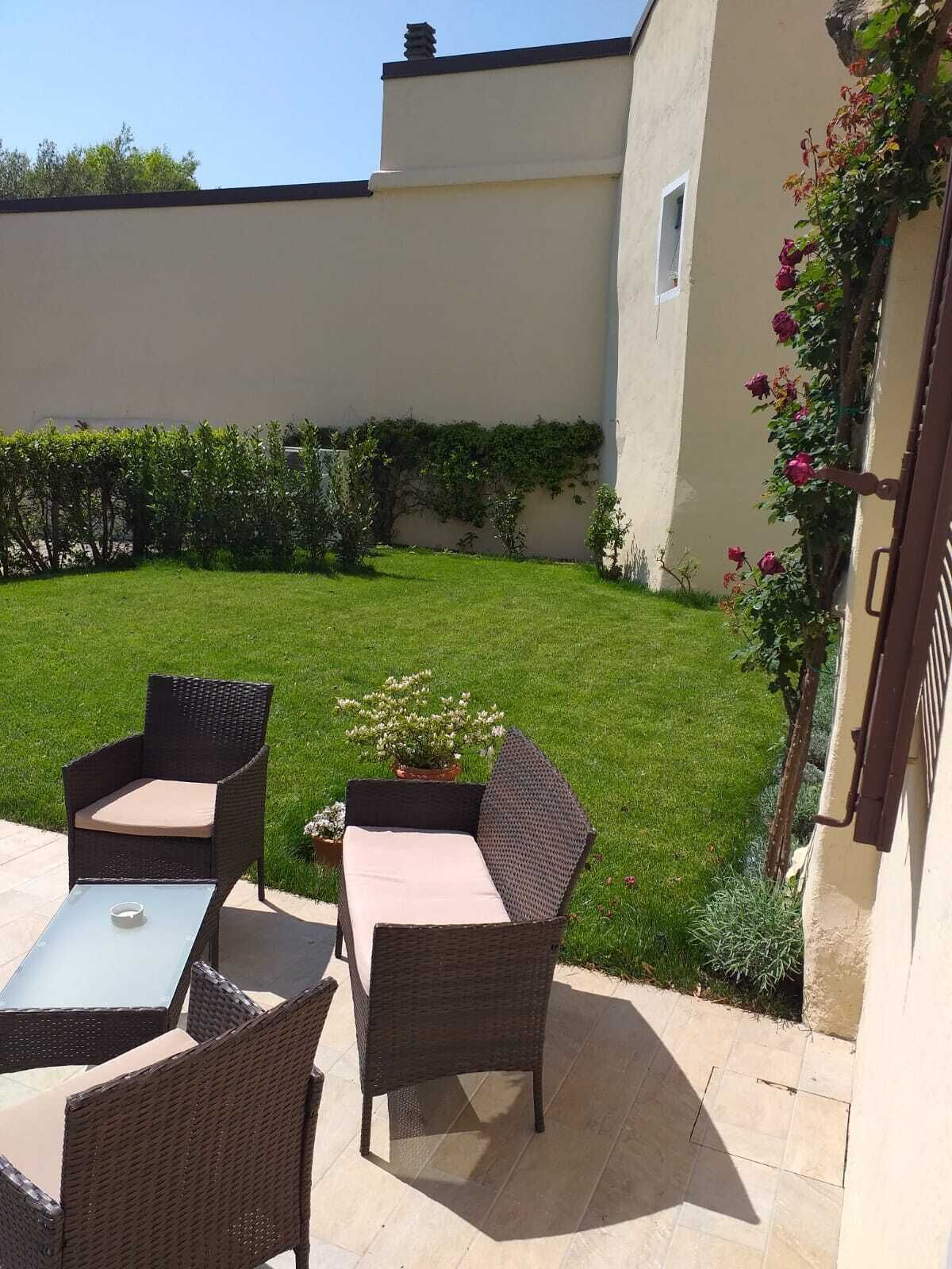 A patio with wicker furniture and a small table, surrounded by a well-maintained lawn and a building with a white exterior.