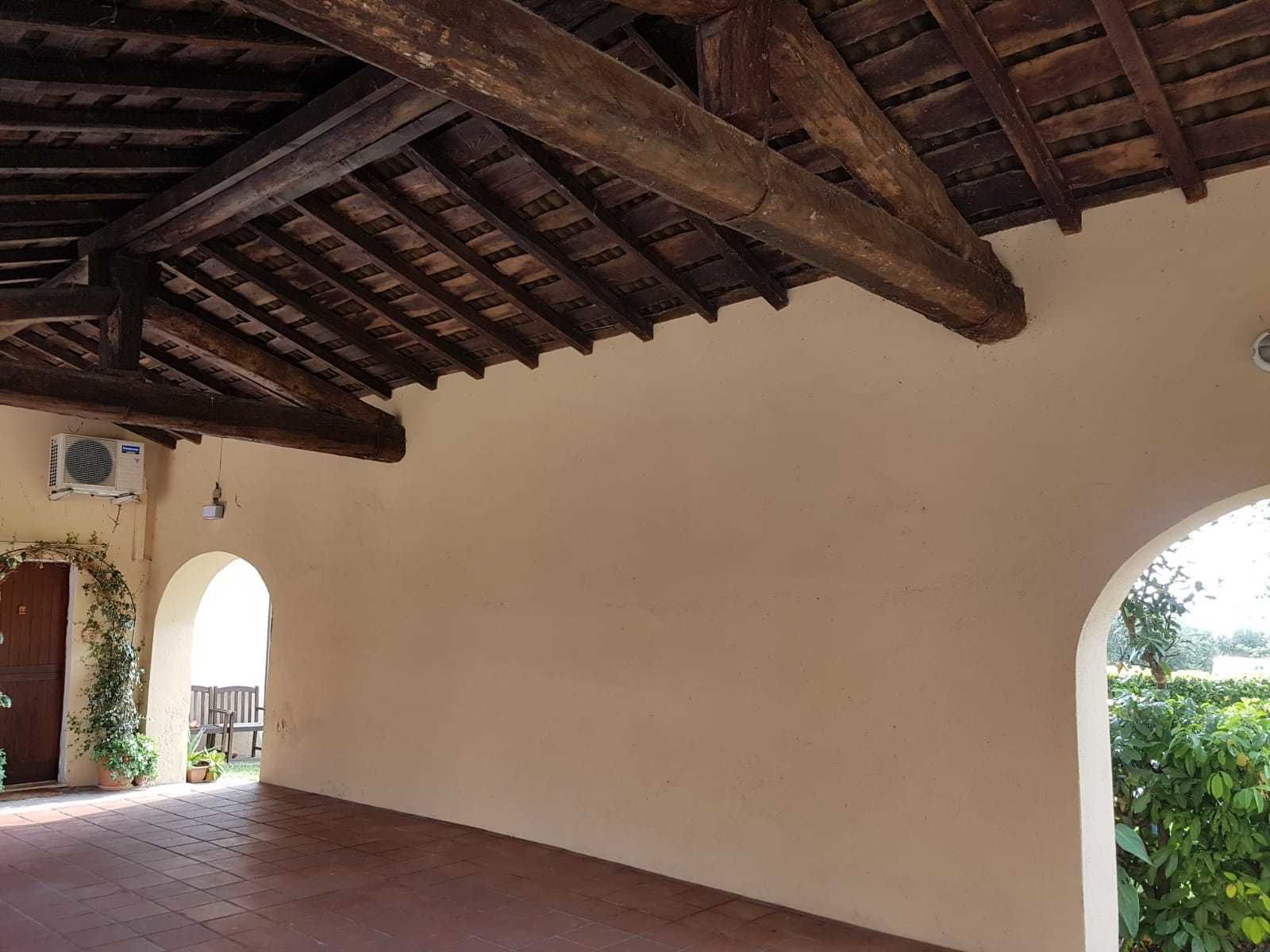 Un espacio exterior techado con suelo de baldosas, vigas de madera y una puerta decorada con una planta.